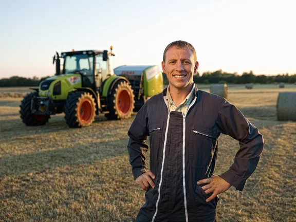 Mann in Arbeitsanzug auf einem Feld vor einem großen Trecker