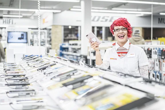 Frau mit Handy in der Hand steht in einem Laden bei vielen Handys