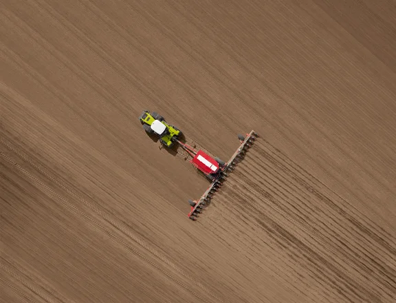 Trecker fährt über ein braunes Feld, von oben