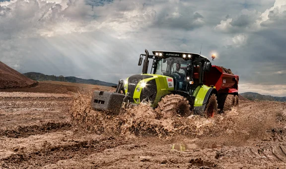 Traktor mit Anhänger fährt durch Matsch der an den Rädern hochspritzt